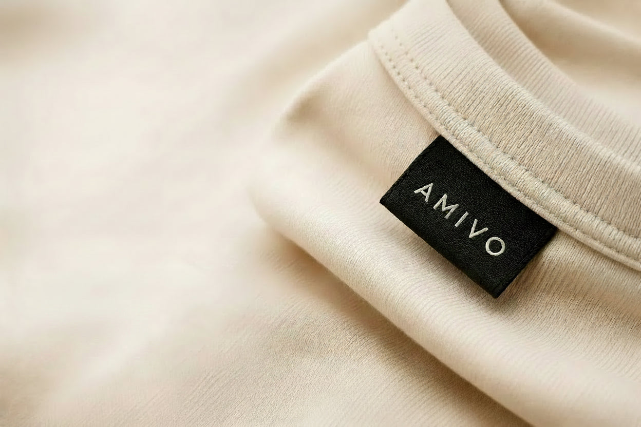 Close-up of a beige or cream ribbed garment with a black AMIVO brand tag, alongside promotional text reading 'Craftsmanship you can feel.' on a matching light background.