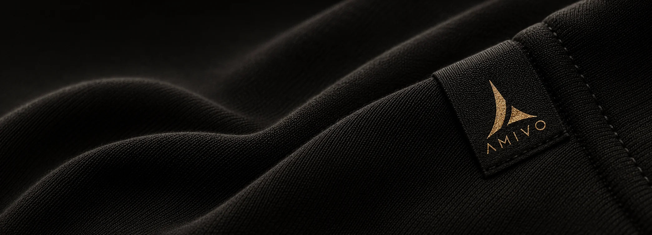 Close-up of a black textured fabric with a small rectangular brand patch reading AMIVO in gold on the right side.